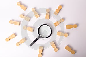 Wooden figures of people lie around a magnifying glass on a white background. The concept of the search for people and workers