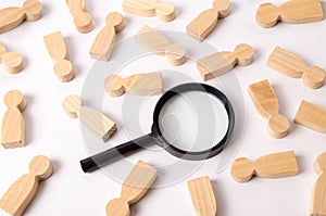 Wooden figures of people lie around a magnifying glass on a white background. The concept of the search for people and workers