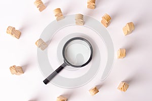 Wooden figures of people lie around a magnifying glass on a white background. Hiring for work, tracing people.