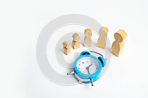 Wooden figures of people from small to large stand around the blue alarm clock. The concept of self-development, growth of persona