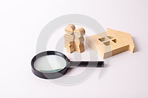 Wooden figures of people are standing near a wooden house and a magnifying glass. The concept of home search, buying and selling.