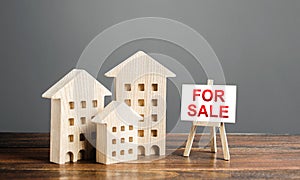 Wooden figures of residential buildings and an easel sign labeled for sale. Buying and selling real estate, hot offers and