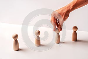 Wooden figures on a white background stand in a row and their male hand moves. The concept of subordination and management, copy s