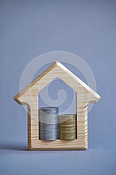 Wooden figurine of house and two columns of coins inside on gray background, the concept of buying or renting a building, eco-