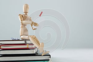 Wooden figurine sitting on a pile of books writing on a paper