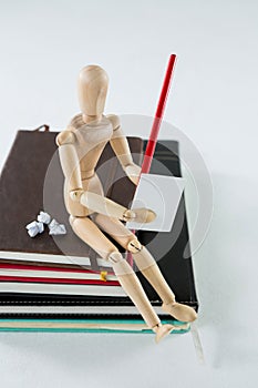 Wooden figurine sitting on a pile of books writing on a paper