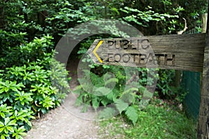 Wooden fingerpost public footpath sign pointing towards a path that goes off into a wood photo