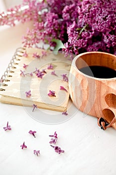Wooden finnish cup with coffee on the table. Nearby lies a closed notebook for notes and a bouquet of lilacs. Good morning and goo