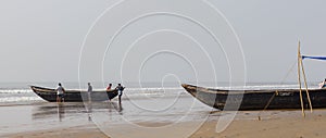 Wooden fishing boat being taken ashore by local fishermen after voyage. Sea waves crashing in the background of the lonely sea