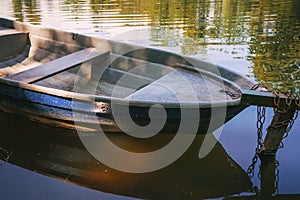 Wooden fishing boat moored with old chain on water surface
