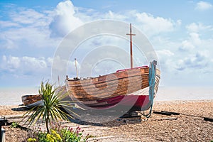 Wooden fishing boat moored on a pebble beach. The mast is in the shape of a cross