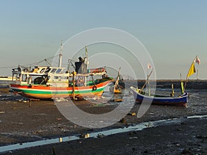 a wooden fishing boat stranded on a beach where the sea water recedes