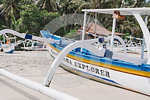 Wooden fishing boat on a virgin beach in Bali. Fishing boats on white sand. Coconut trees on the background.