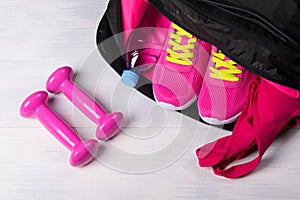 On the wooden floor sports bag with pink things in it uncovered, and two dumbbells