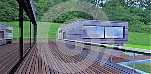 Wooden flooring on the terrace with glass railing. Large sliding windows reflect the environment. 3d rendering