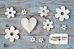 Wooden flowers, heart, black chalk board and thank you label on a blue grey knotted old wooden background with empty space layout