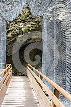 A wooden footbridge over a mountain river. A steel mesh protects the passage against possible falling stones