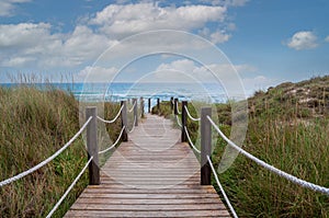 Wooden footbridge between sand dunes to the beach and ocean at menorca spain