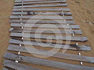 Wooden footbridge on a sandy beach. Uneven, damp wooden planks held together. The edge of the beach season at the hotel