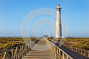 Wooden footbridge walkway to beach near Morro Jable lighthouse in warm sunset light, Fuerteventura island, Spain