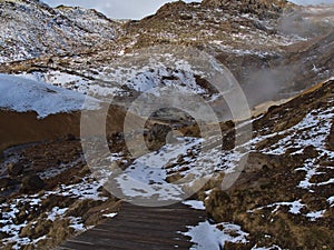 Wooden footpath leading through geothermal area SeltÃºn with hot springs, fumaroles and mud pots in Iceland.