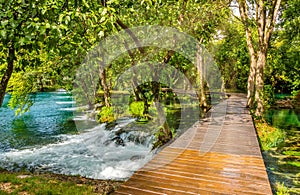 Wooden footpath over river in forest of Krka National Park, Croatia. Beautiful scene with trees, water and sunrays.