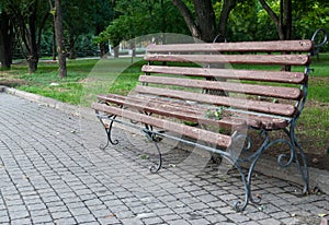 Wooden forged park bench, brown bench with forged metal legs, pavement tiles, park square