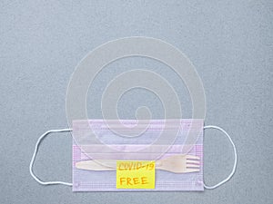 Wooden fork, pink medical mask and sticker with the inscription covid-19 free. photo