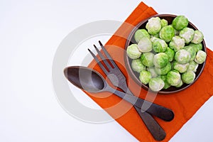 Wooden fork and spoon lie on the table, next to ripe Brussels sprouts lies in a wooden bowl on a tablecloth