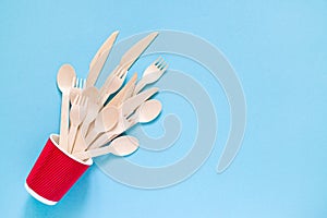 Wooden forks, spoons and knives in a red paper glass against blue background