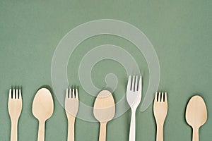 Wooden forks, spoons and one plastic fork on a green background. Eco-friendly disposable tableware. Refusal of plastic