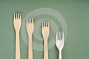 Wooden forks, spoons and one plastic fork on a green background. Eco-friendly disposable tableware. Refusal of plastic