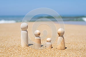 Wooden four figures of people on the sand of beach with sea view. Concept of happy family with two kids on holiday.