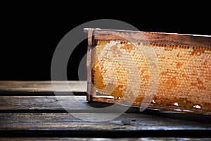 Wooden frame with honeycomb full of honey, on black