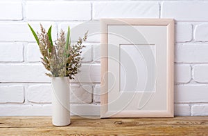 Wooden frame mockup with grass and green leaves in cylinder vase