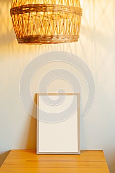 A wooden frame stands on a table illuminated by a yellow lamp made of natural materials. a place for your design and photos