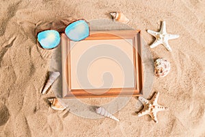 Wooden frame, sunglasses and seashells on sand beach