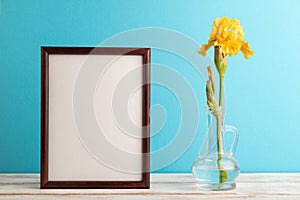 Wooden frame with yellow iris flower in glass on blue pastel background. side view, copy space