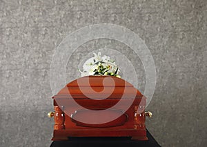 Wooden funeral casket with white lilies at grey