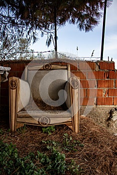 Wooden furniture made of natural materials in the garden. Abandoned old armchair on the beach near the brick wall.