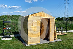 A wooden garden shed under construction standing on a concrete foundation in the garden, visible greenhouse.