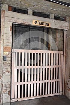 The wooden gate is closed to a very old freight elevator in an old warehouse building.