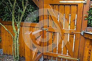 Wooden gate and fence on the back of the home garden. The gate is closed with a padlock.