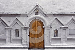 Wooden gate and two arched windows on a white brick wall. Entrance to the old christian church