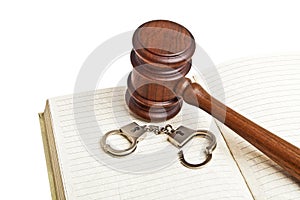 Wooden gavel, notebook and handcuffs on white background