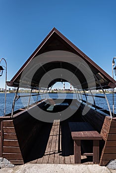 A wooden gazebo in the shape of a boat with a deck near the river