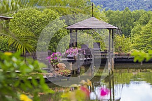 Wooden gazebo with sun loungers for relaxing on a terrace with flowers next to a lake on the tropical island of Thailand
