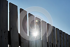 Wooden gray fence on a sunny summer day. The sun shines through the fence