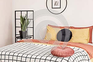 Wooden grille next to the bed with orange bedding in the bedroom with white walls