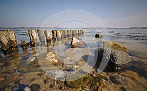 Wooden groyne leading out to sea with shallow water and rocks in the foreground long exposure